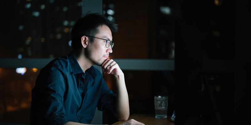 Man sitting at a desk at night looking at a computer monitor.