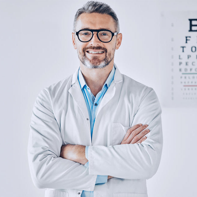 Optometrist in a white coat standing in front of an eye chart.