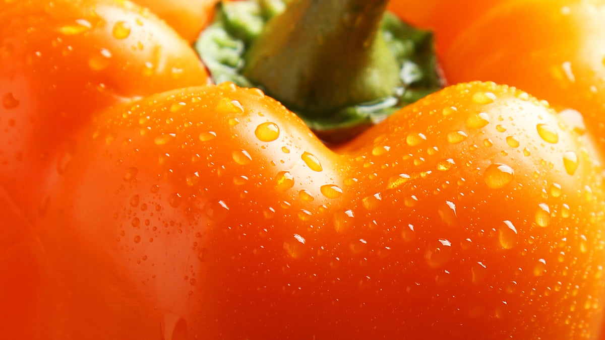 Close-up of a bright orange pepper with water droplets on its surface.
